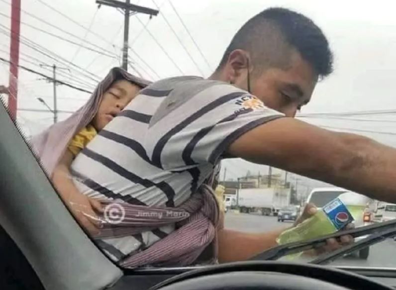 Gran ejemplo, un joven limpia parabrisas cargando a su bebé